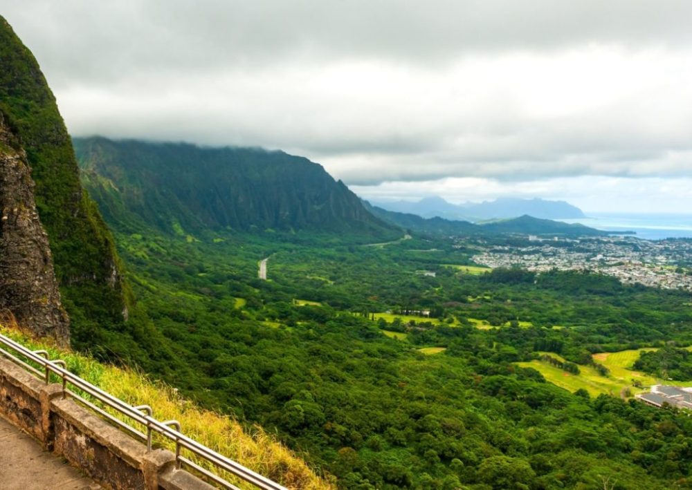 a train traveling through a lush green hillside with Nu‘uanu Pali in the background