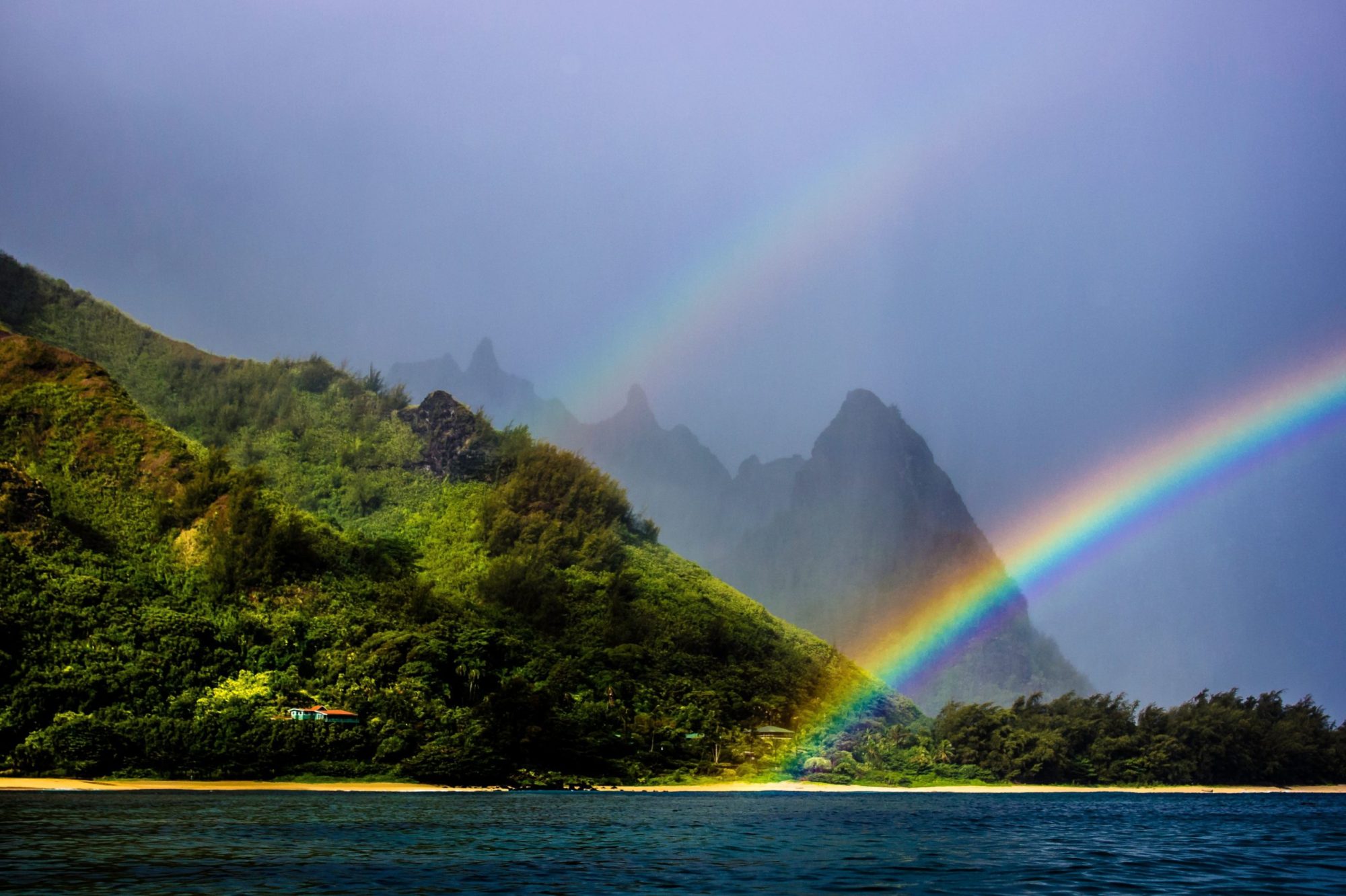 Rainfall in Kauai creates rainbows a rainbow over a body of water with a mountain in the background