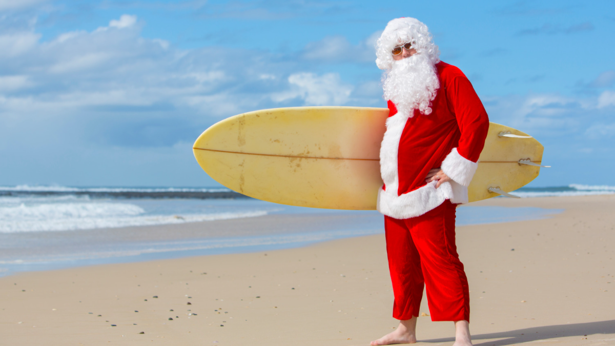 santa a person standing on a beach holding a surfboard