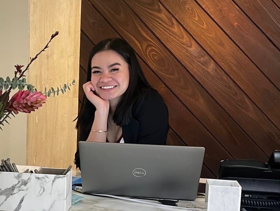 a woman sitting at a table with a laptop and smiling at the camera