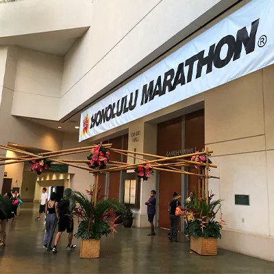 Entrance with Honolulu Marathon banner and floral decorations, people gathered below.