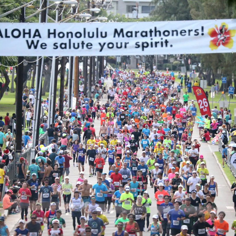 Large crowd of marathon runners under a banner in Honolulu.