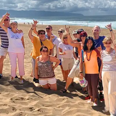 Group of smiling people posing on a beach with ocean waves in the background.