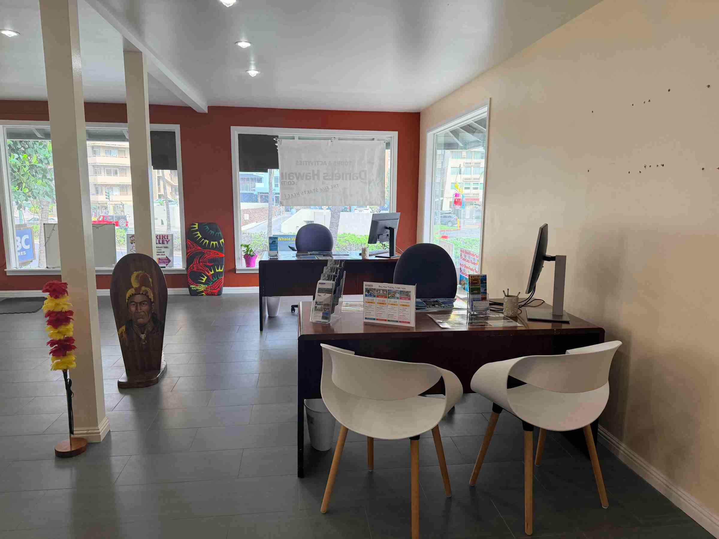 Office with desks, chairs, and decorative items near large windows with blinds.
